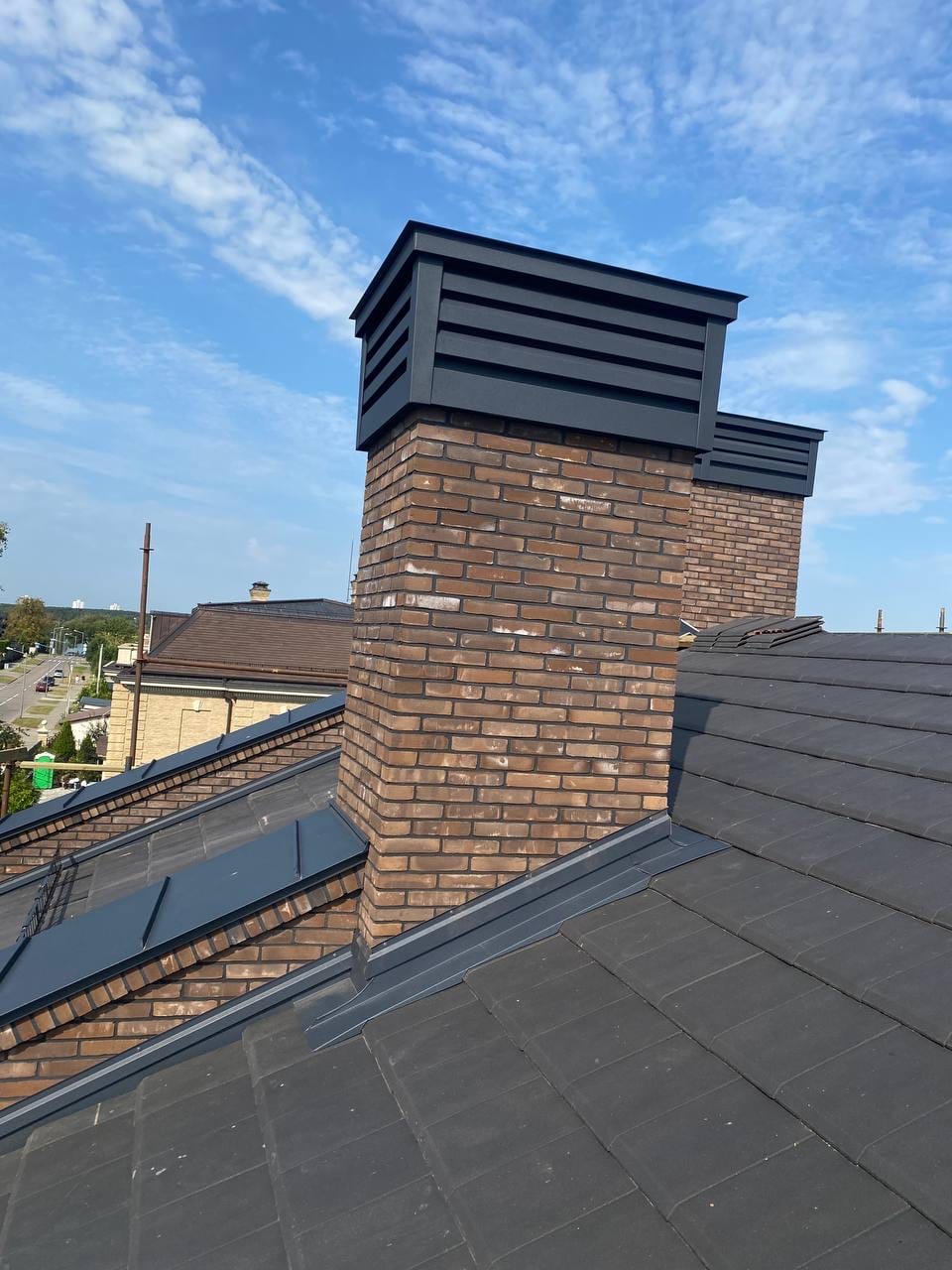 Powder-coated steel chimney cap with louvered vents and matching step flashing on a brick chimney